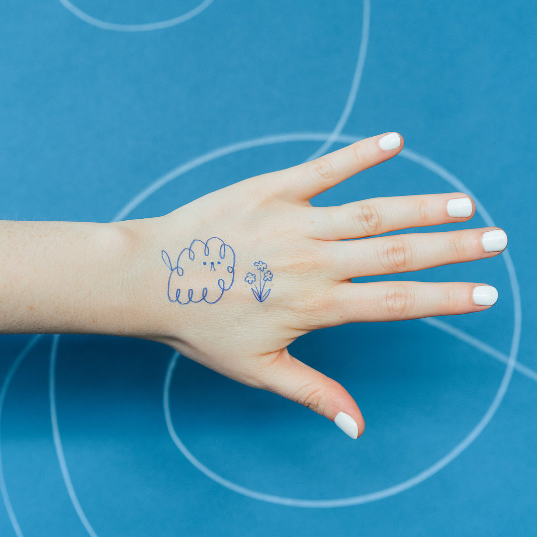 Blue Outline Scribble Dog And Scribble Flower Tattly Temporary Tattoos On A Person's Hand